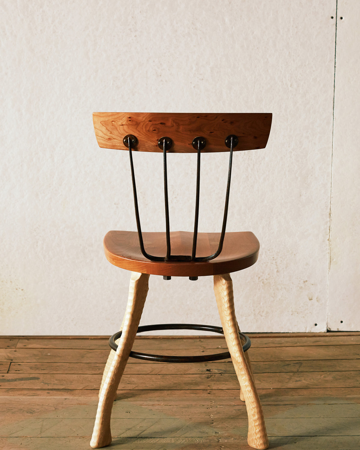 Rear view of the 18" dining height Pitchfork Chair showing four forged pitchfork tines connecting the solid cherry seat to the cherry backrest, with round steel caps where the tines meet the backrest rail. Ax handle lathe-turned ash legs and steel hoop stretcher visible below.