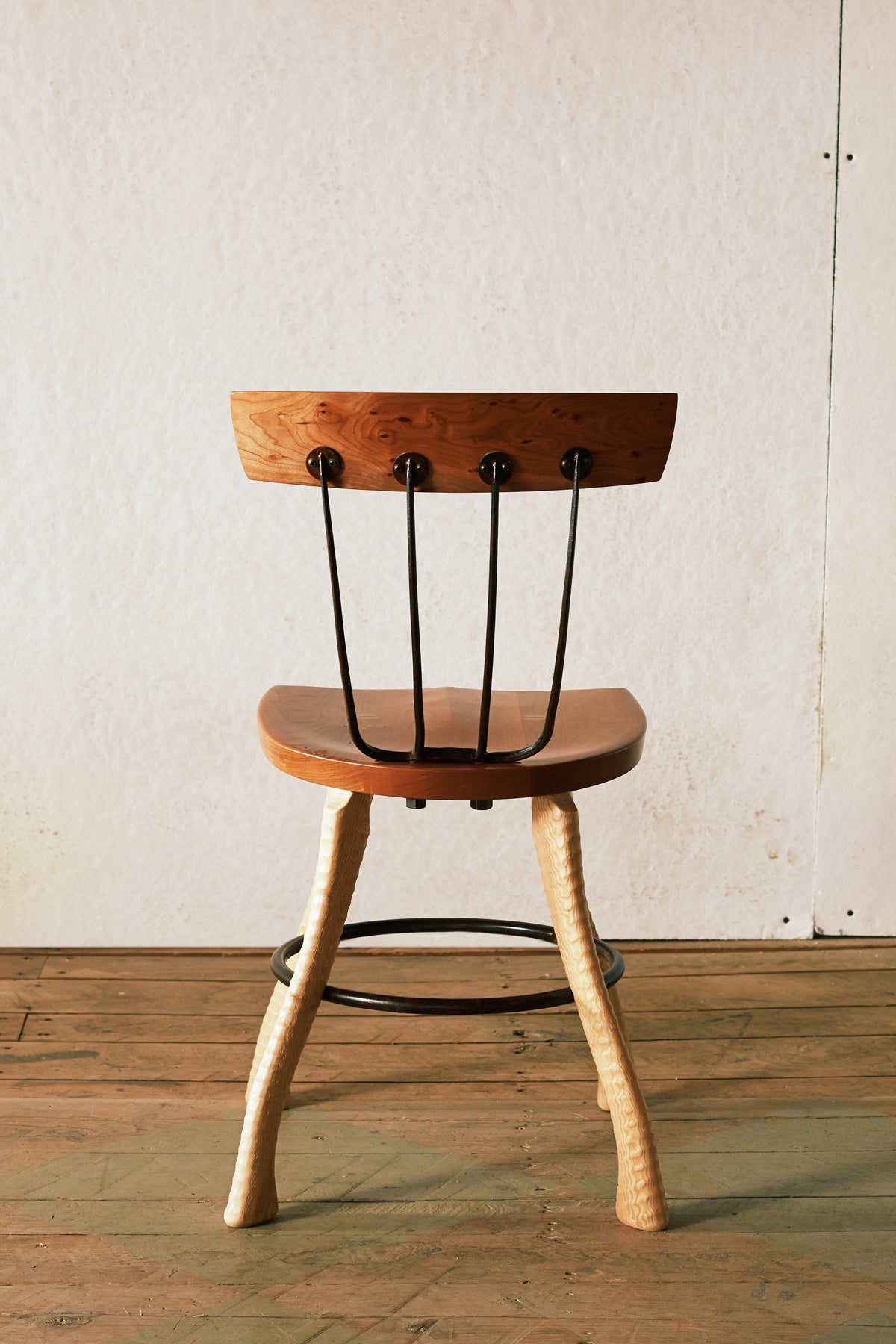 Rear view of the 18" dining height Pitchfork Chair showing four forged pitchfork tines connecting the solid cherry seat to the cherry backrest, with round steel caps where the tines meet the backrest rail. Ax handle lathe-turned ash legs and steel hoop stretcher visible below.