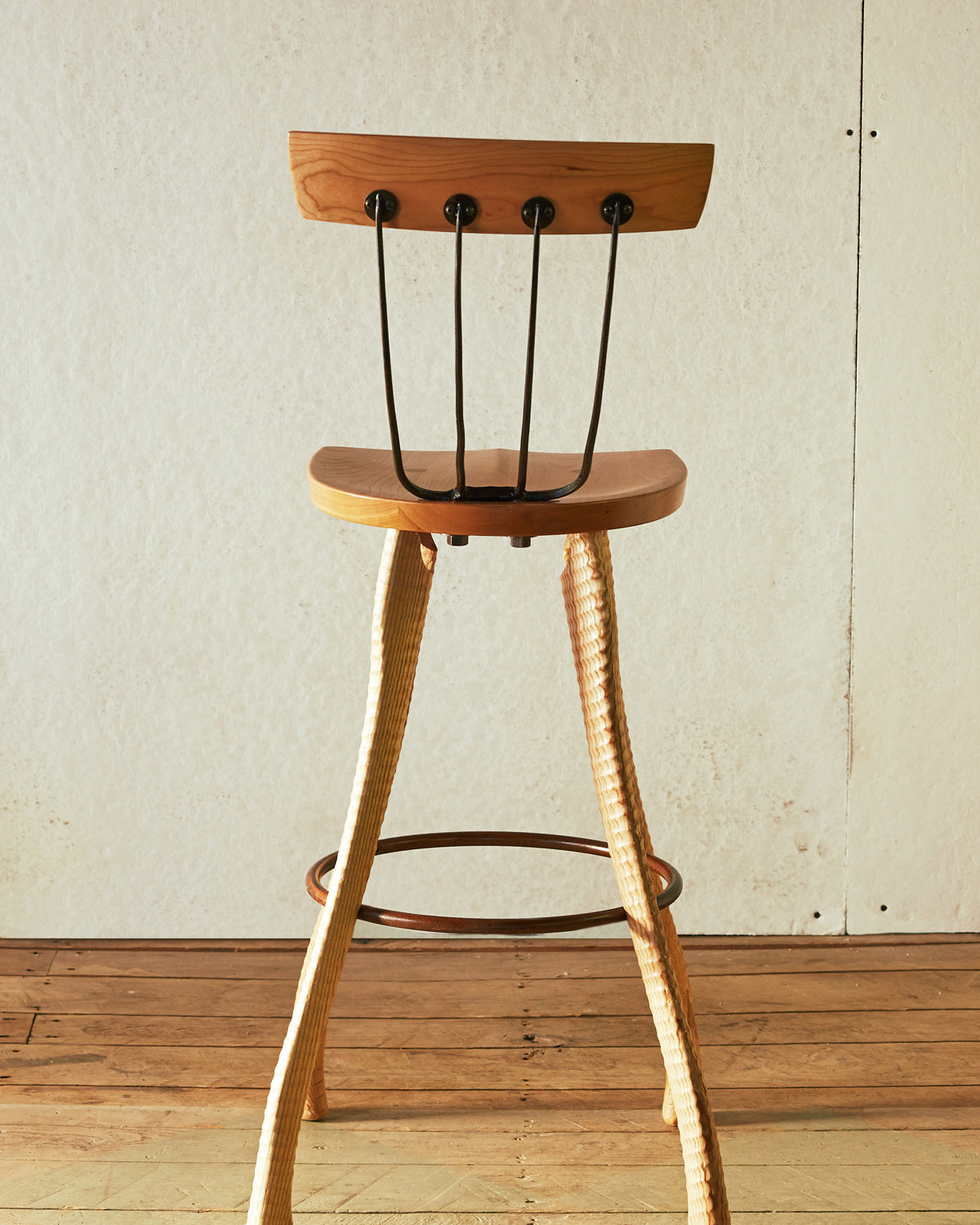 Rear view of the 25" counter height Pitchfork Chair showing the full length of the ax handle lathe-turned ash legs, forged pitchfork tine back spindles with round steel caps, solid cherry backrest, and steel hoop footrest.
