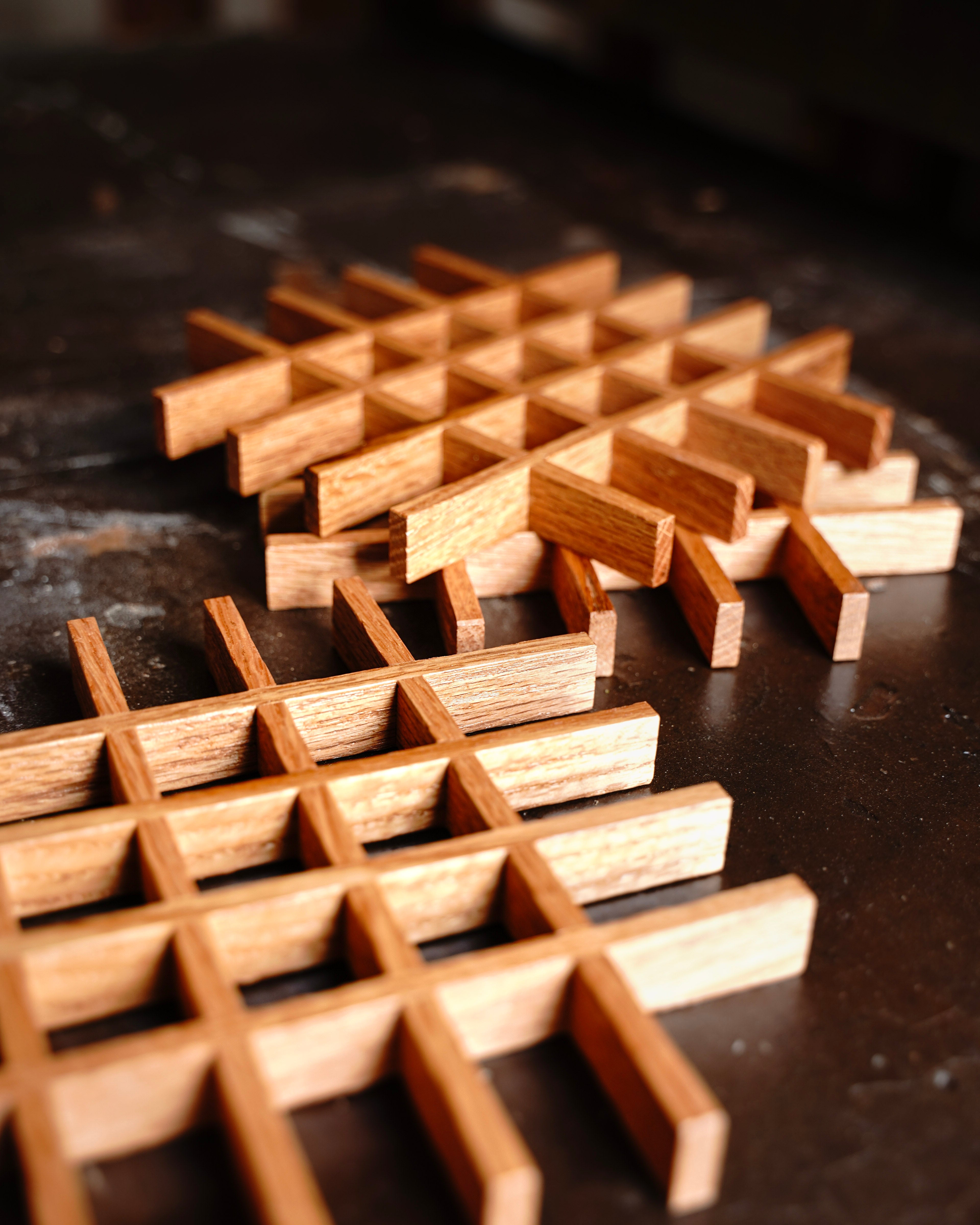 Two handcrafted oak lattice trivets by Bradford Woodworking photographed from above on a rustic wood surface, showing the open grid construction in light and medium oak tones.