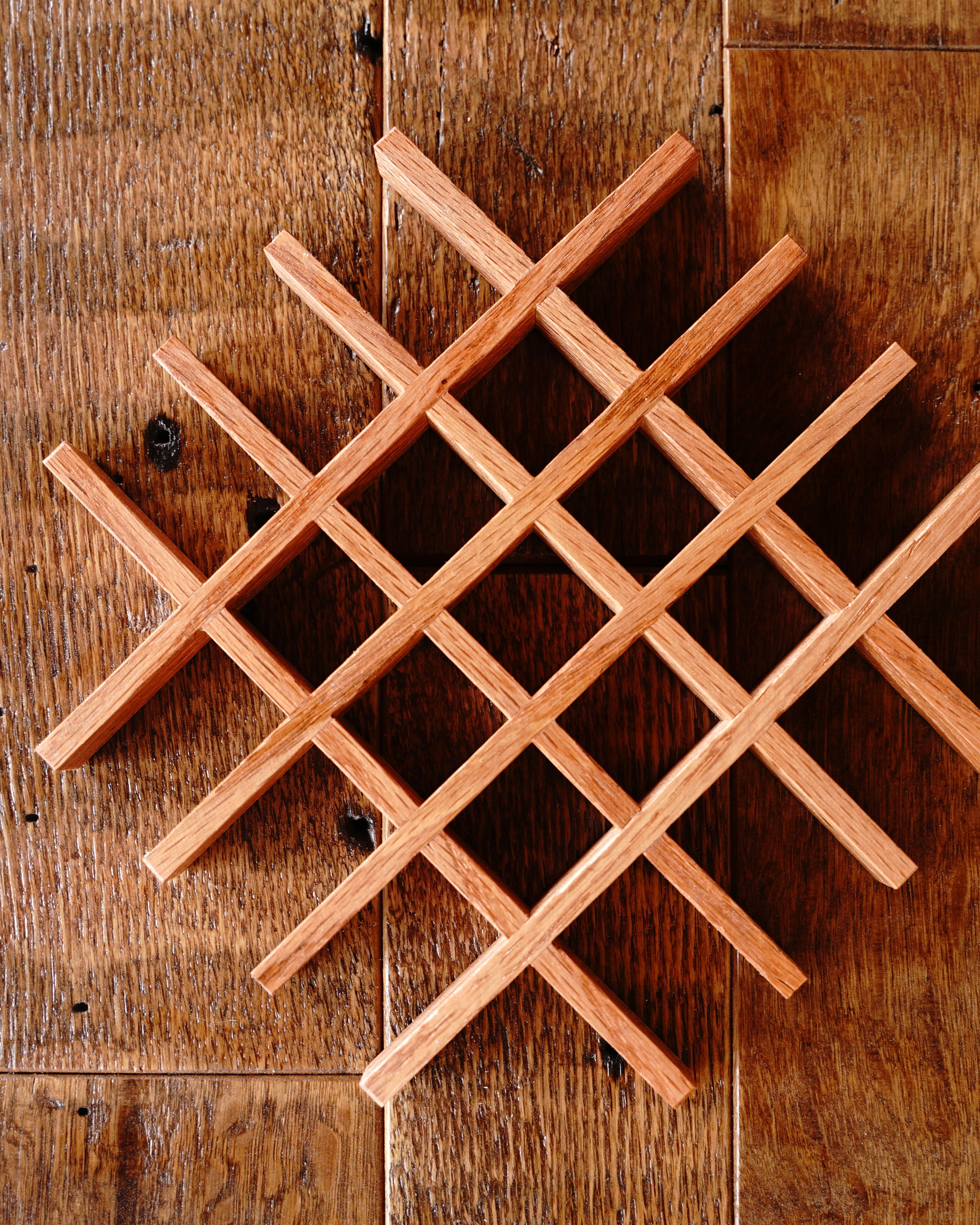Dozens of small handcrafted oak lattice trivet components laid out on a workshop surface at Bradford Woodworking, showing the small-batch production process before final assembly.