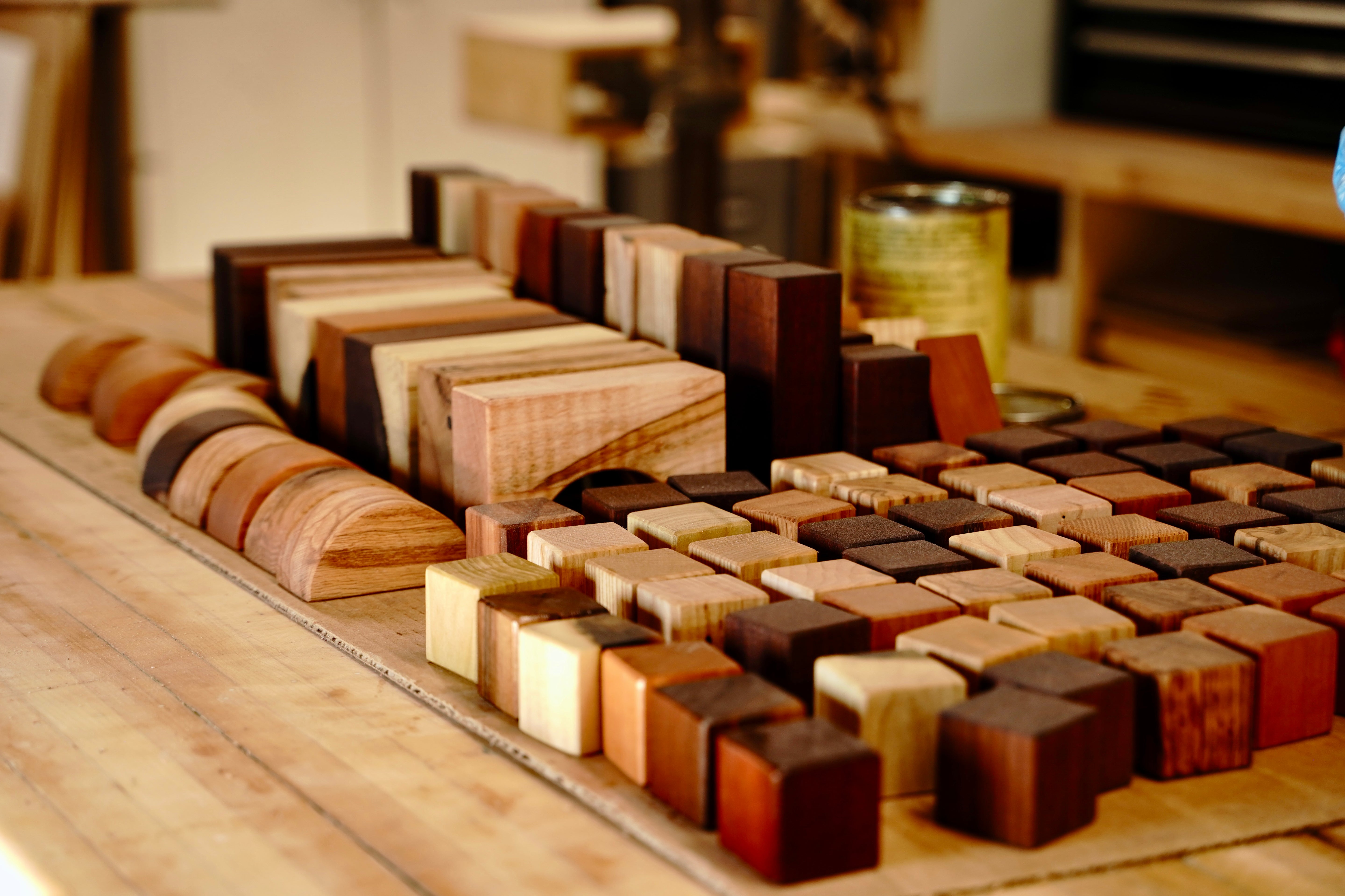 Wide shot of a complete handcrafted baby block set spread across a woodworking workbench, showing the full range of shapes and wood species including cubes, wedges, arches, and stacking blocks in cherry, walnut, maple, oak, ash, and poplar.