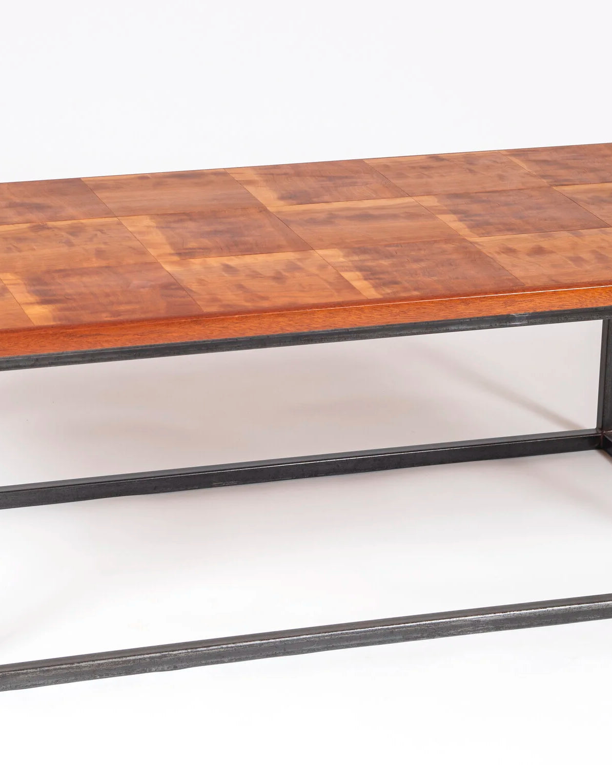 Handcrafted coffee table with a highly figured solid cherry top laid in a tiled panel pattern, showing warm amber and reddish brown tones with natural variation across each section. The base is a clean rectangular welded steel box frame in a dark finish. Photographed against a white background.