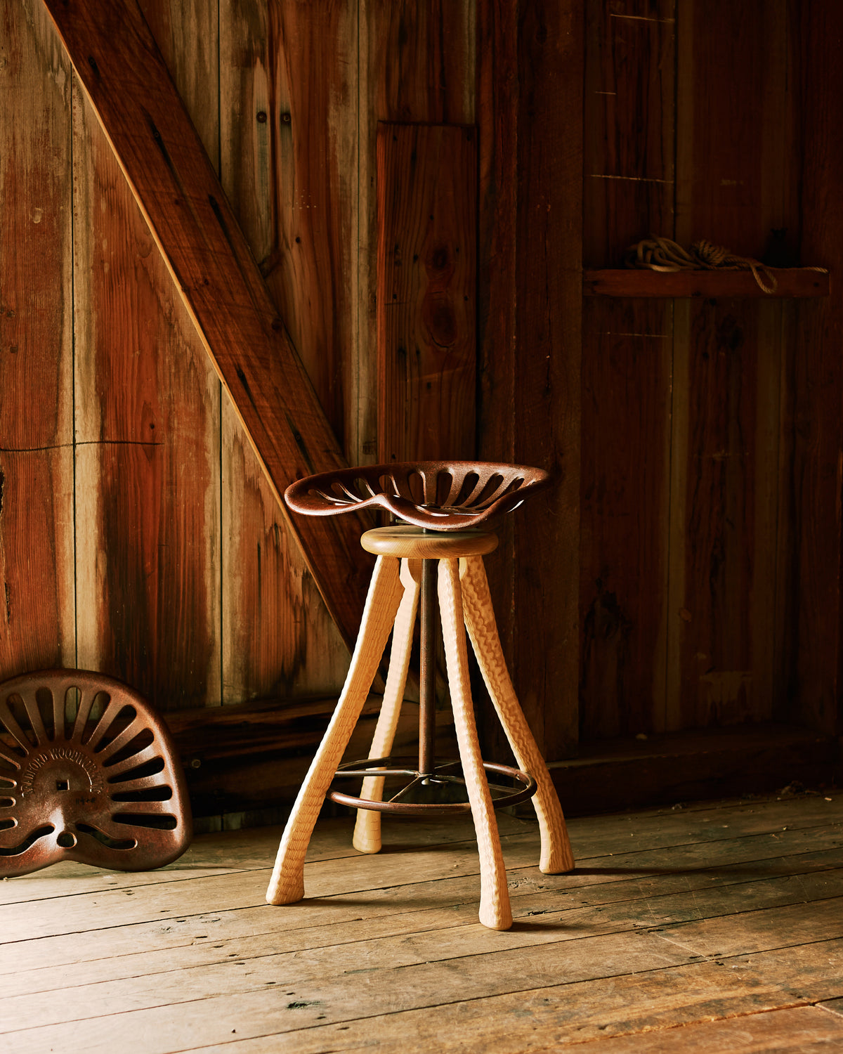 Handmade tractor seat bar stool with cast iron seat and ax handle ash legs, photographed in barn, Bradford Woodworking Worcester PA