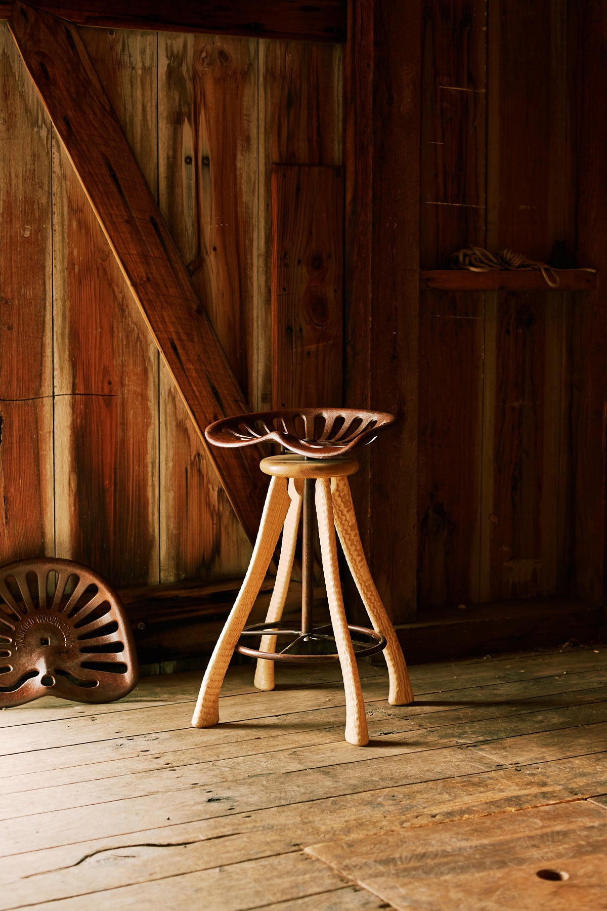 Handmade tractor seat bar stool with cast iron seat and ax handle ash legs, photographed in barn, Bradford Woodworking Worcester PA