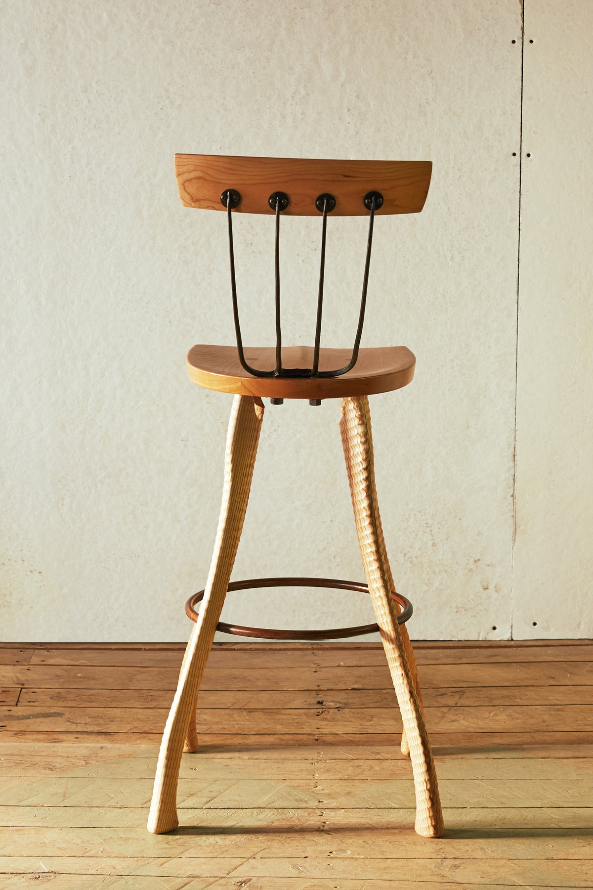 Rear view of the 25" counter height Pitchfork Chair showing the full length of the ax handle lathe-turned ash legs, forged pitchfork tine back spindles with round steel caps, solid cherry backrest, and steel hoop footrest.