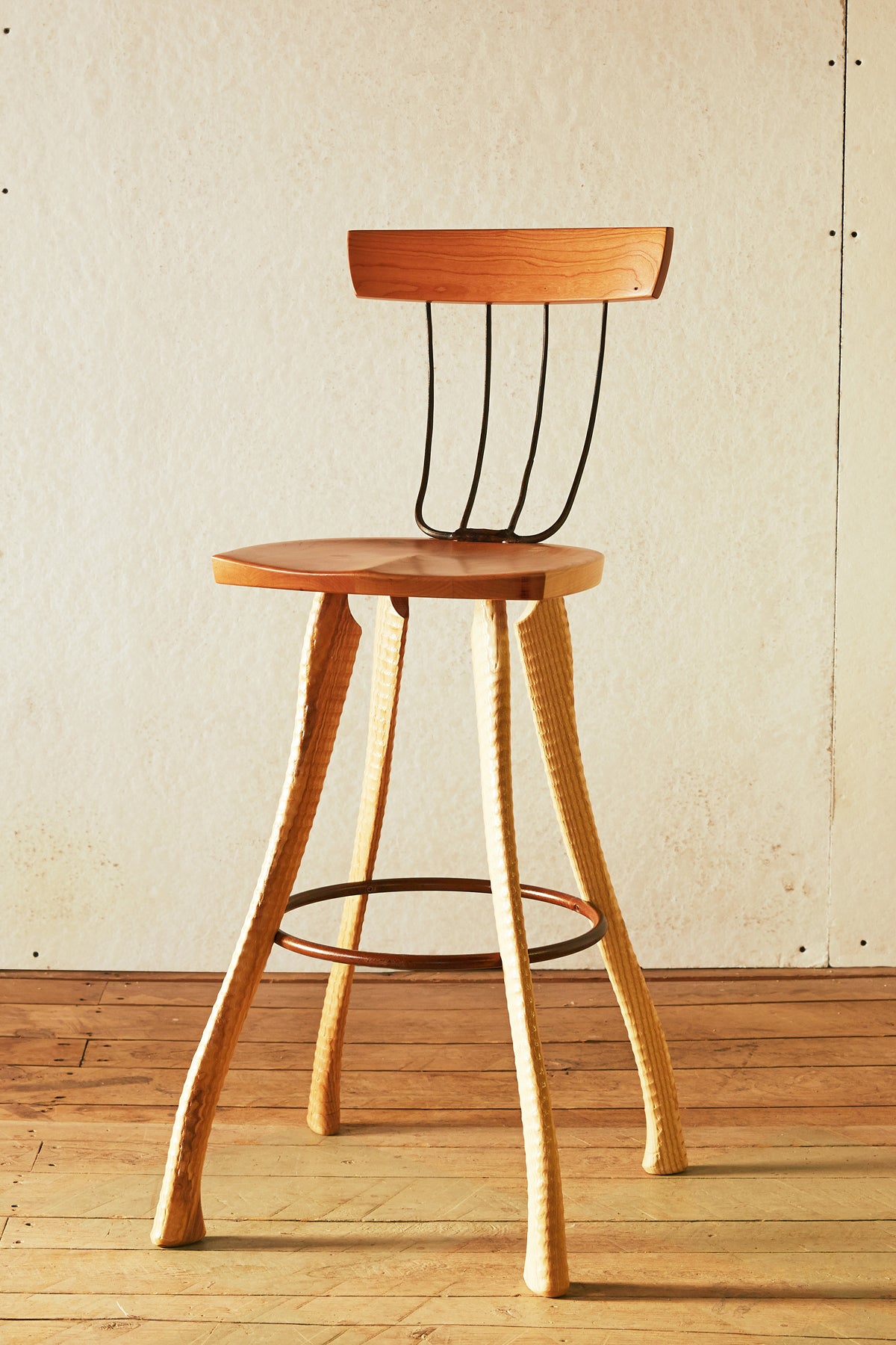 Front view of the Bradford Woodworking Pitchfork Chair at counter height. Solid cherry round seat and backrest, four forged steel pitchfork tine spindles, ax handle lathe-turned ash legs splaying outward, and a steel hoop stretcher at footrest height.