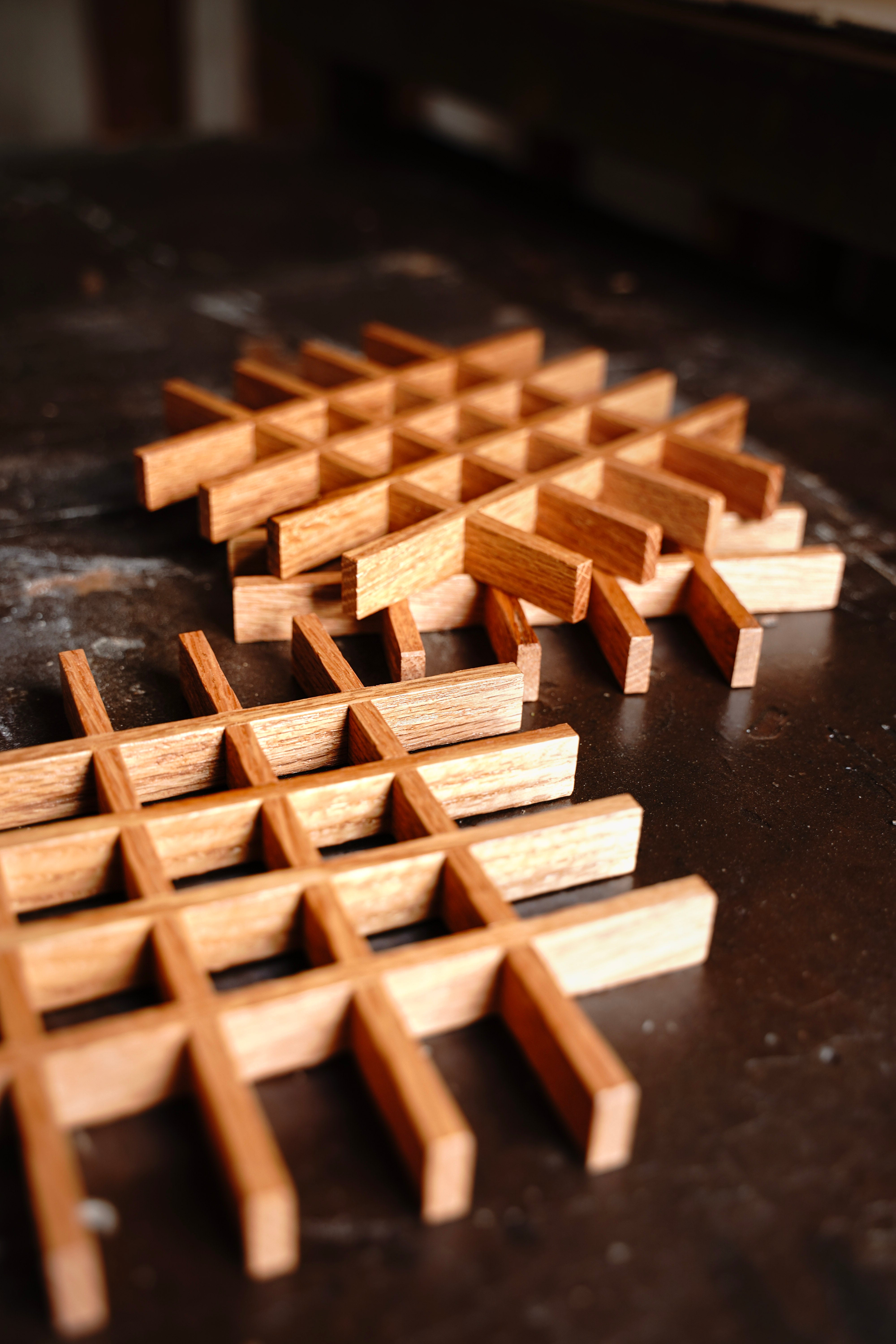 Two handcrafted oak lattice trivets by Bradford Woodworking photographed from above on a rustic wood surface, showing the open grid construction in light and medium oak tones.