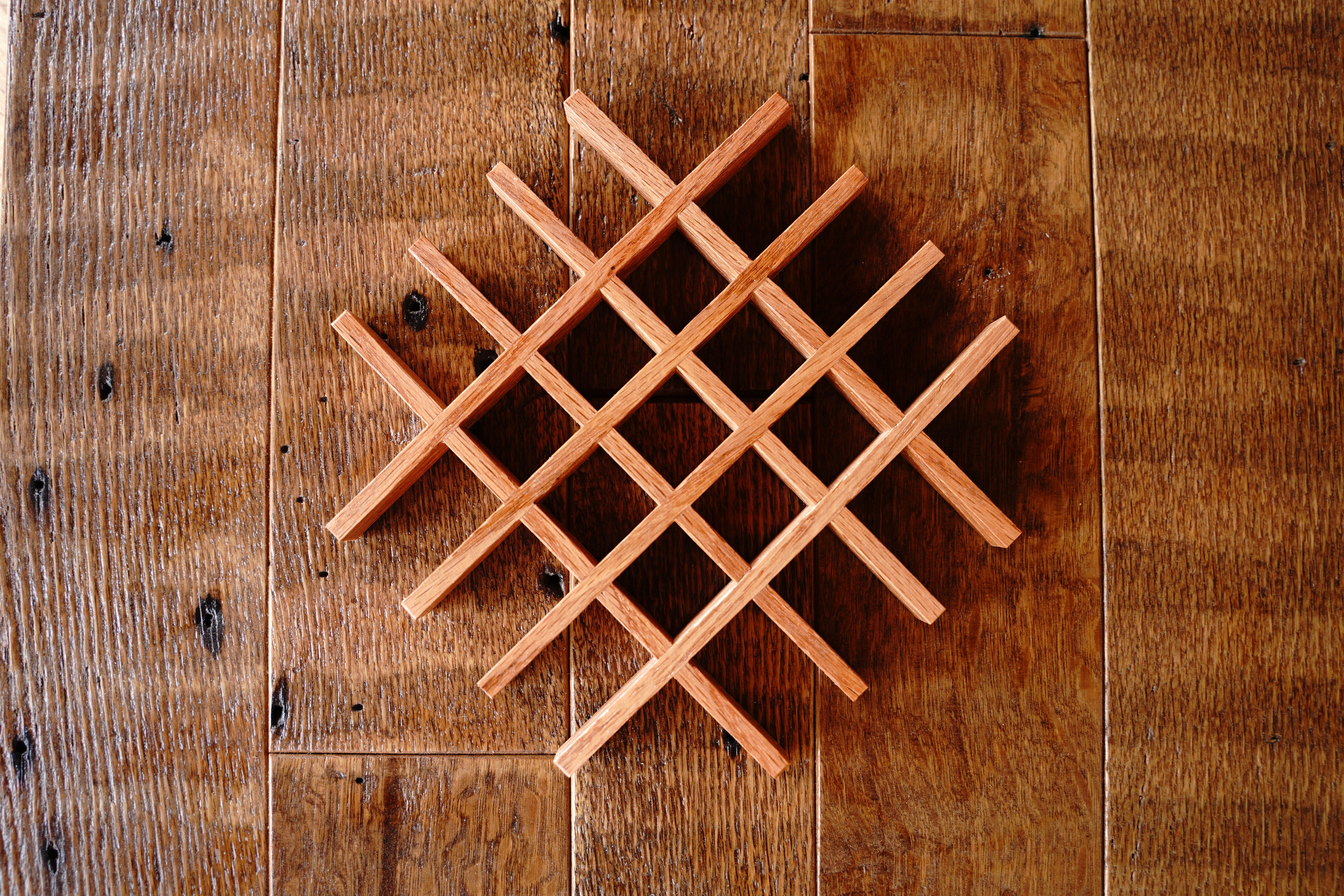 Dozens of small handcrafted oak lattice trivet components laid out on a workshop surface at Bradford Woodworking, showing the small-batch production process before final assembly.