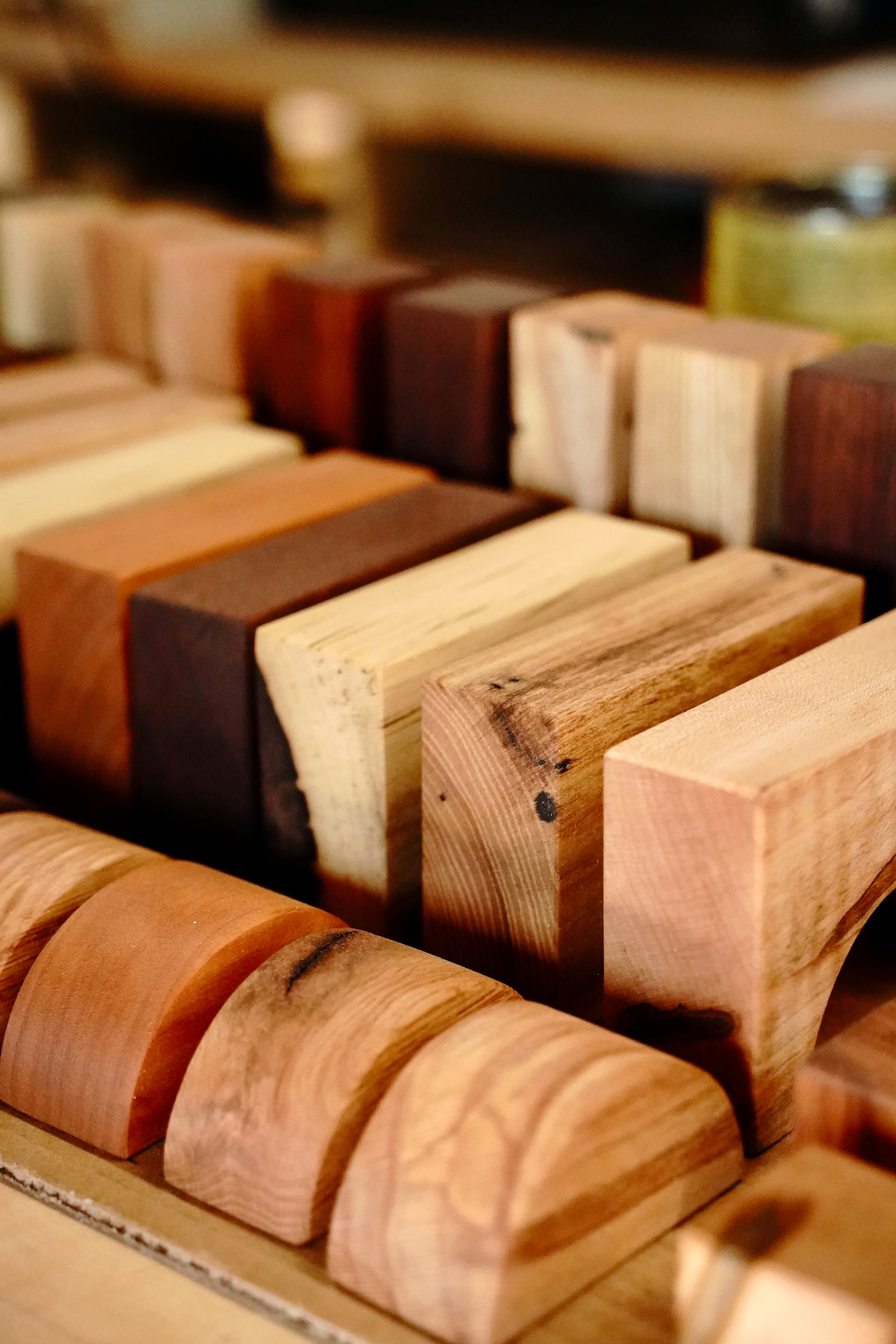 Detail shot of handcrafted hardwood baby blocks showing the natural color range created by using multiple wood species. Blocks in light ash and maple sit alongside deep walnut and warm cherry, with visible wood grain on every piece.