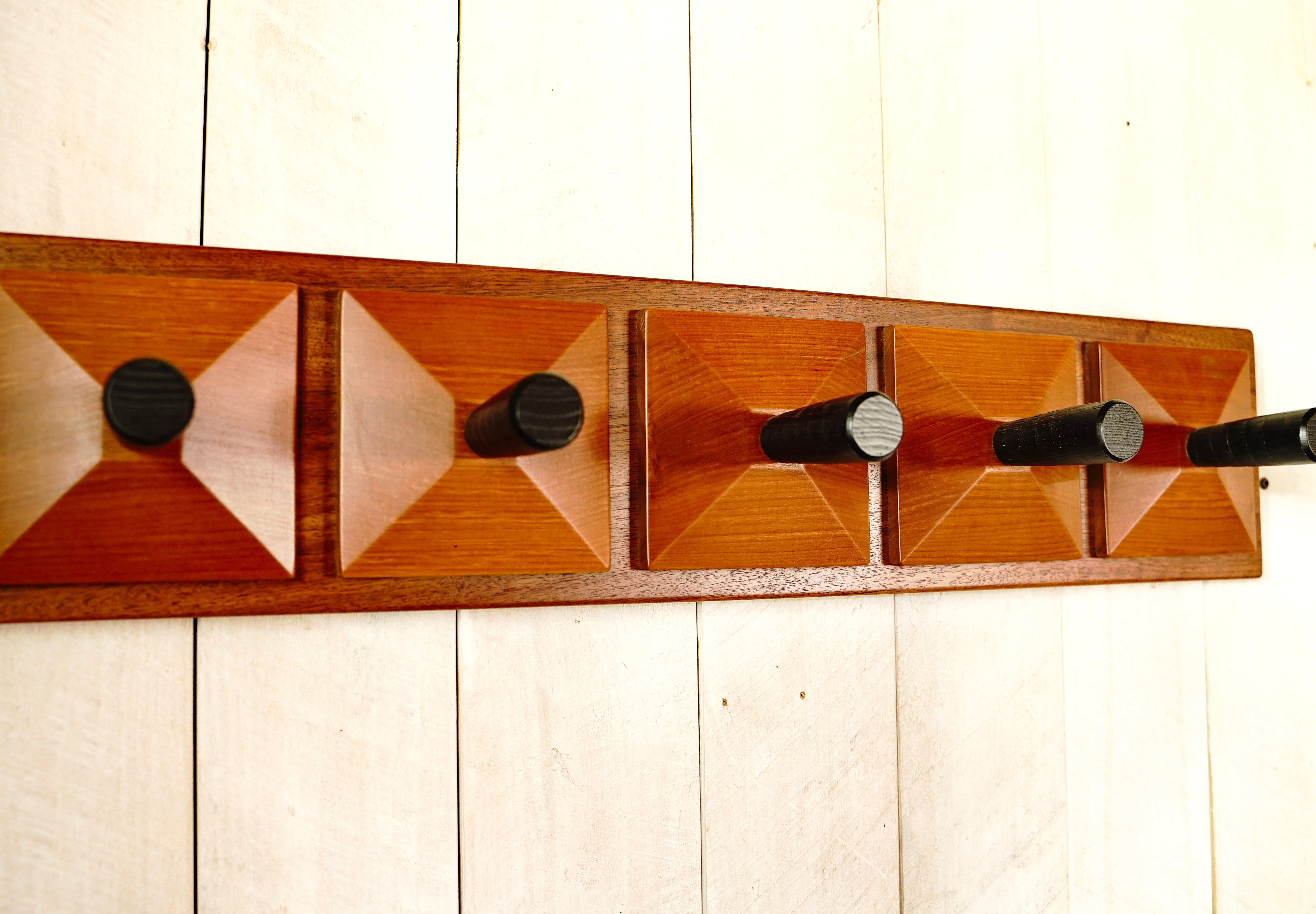 Close-up of hand-carved redwood pyramid facets and black maple pegs on a handmade walnut coat rack.