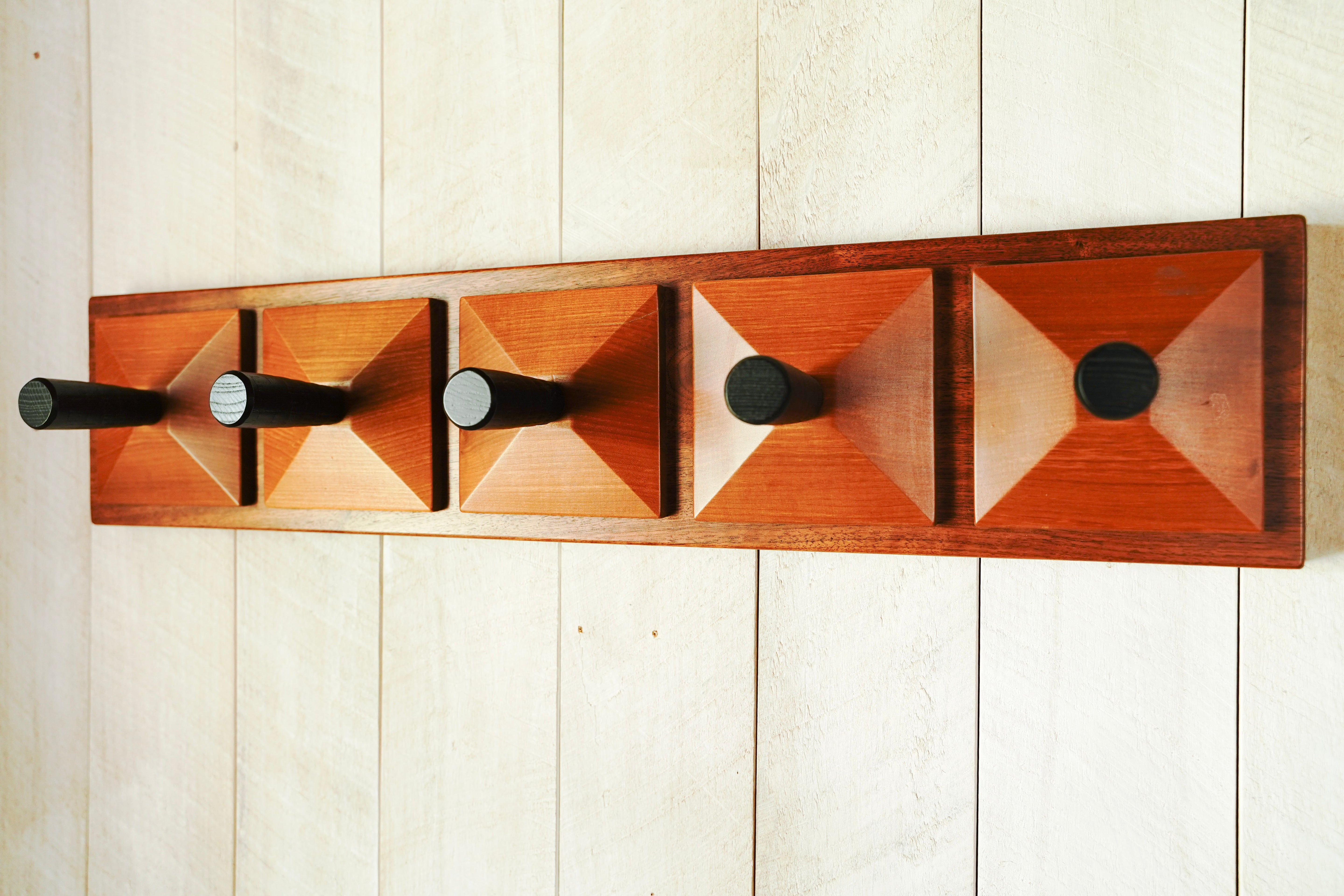 Side angle of a handmade redwood and walnut coat rack showing dimensional pyramid detail and black wood hooks