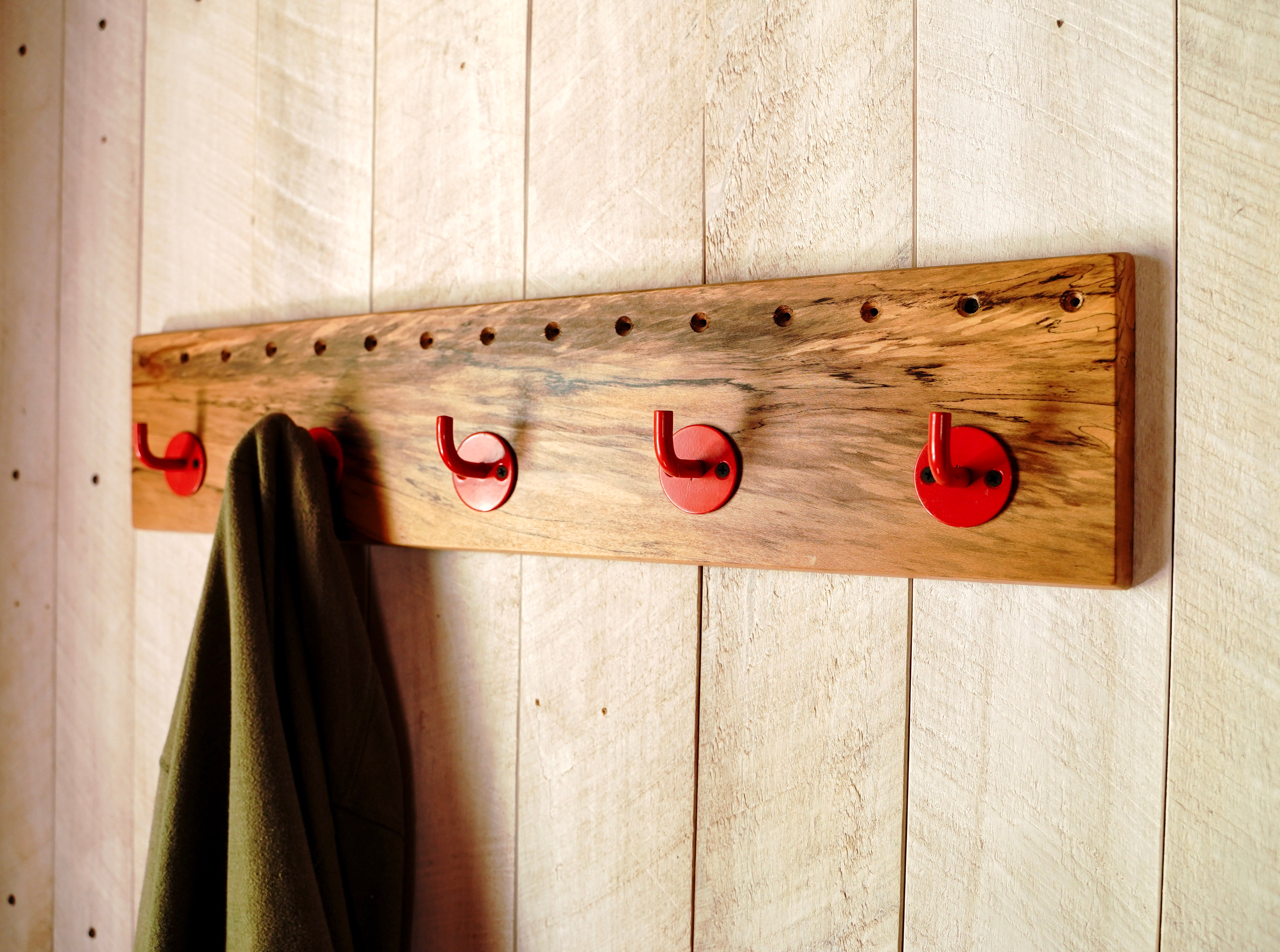 Close-up angle of spalted maple grain and red steel hooks on a handmade wall-mounted coat rack