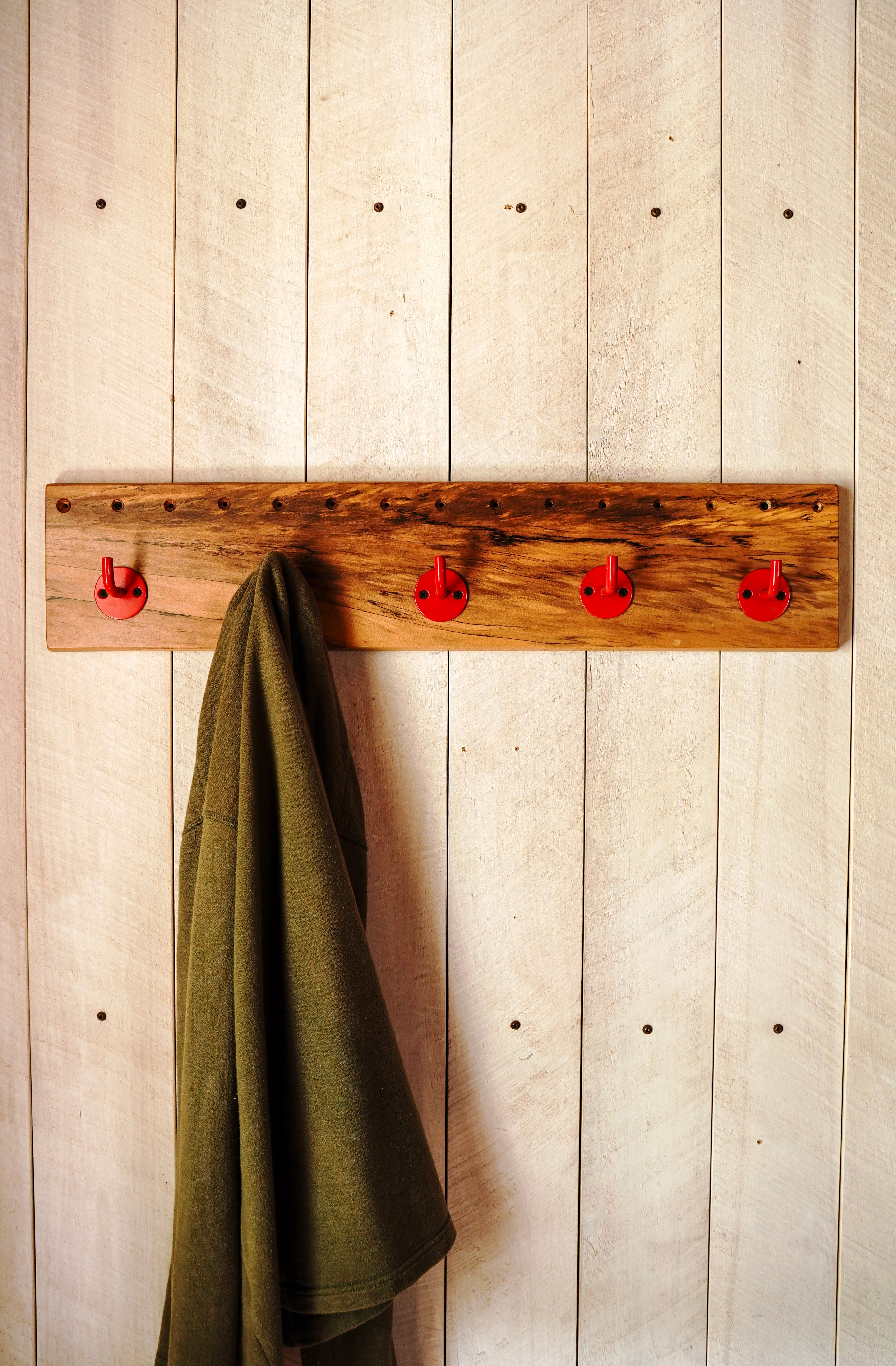 Spalted maple coat rack with red steel hooks, styled with a sweater hanging in an entryway