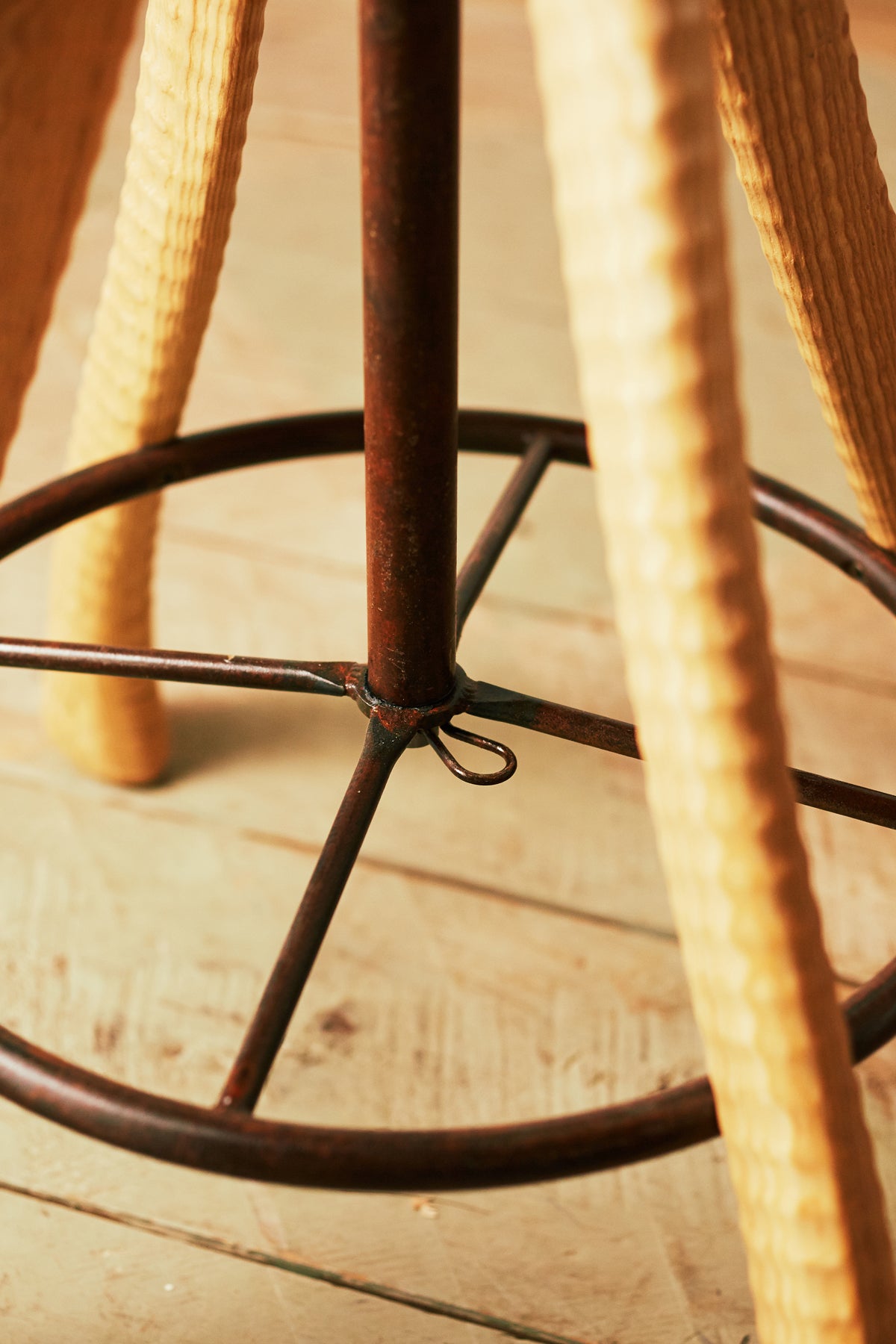 Detail of hand-bent iron footrest ring and central swivel post on Bradford Woodworking tractor seat stool
